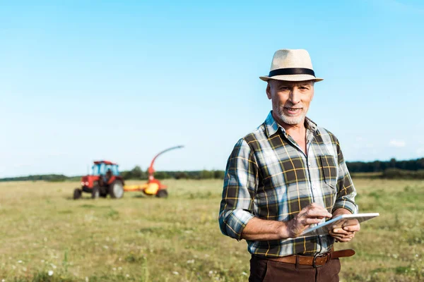 Granjero alegre en sombrero de paja utilizando tableta digital en el campo - foto de stock