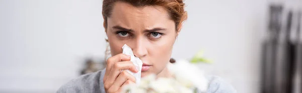 Panoramic shot of sick woman with pollen allergy holding tissue near flowers — Stock Photo