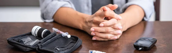 Colpo panoramico di donna seduta con le mani serrate vicino al kit di pronto soccorso e alla siringa — Foto stock