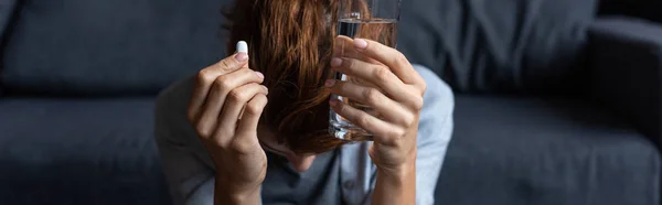 Панорамний знімок хворої жінки, що тримає таблетку і склянку води вдома — стокове фото