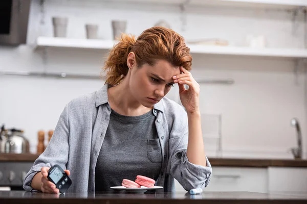 Mujer molesta con alergia dulce sentado cerca de postre y monitor de glucosa - foto de stock