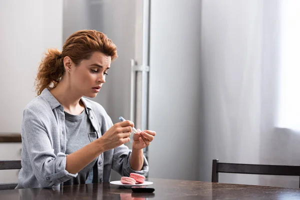 Verärgerte Frau mit süßer Allergie sitzt in der Nähe des Desserts und schaut auf Blutlanzette — Stockfoto