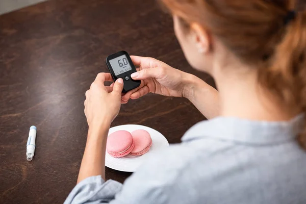 Concentrazione selettiva della donna che tiene il monitor del glucosio vicino al dolce dessert — Foto stock