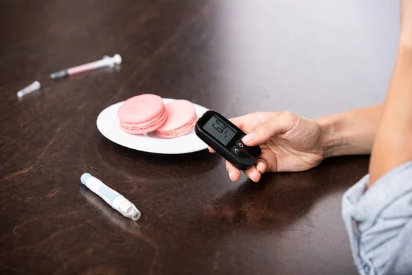 Ausgeschnittene Ansicht einer Frau mit einem Glukosemesser in der Nähe eines süßen Desserts — Stockfoto
