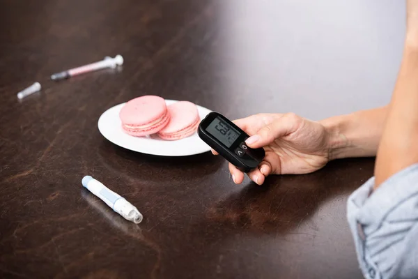 Vista recortada de la mujer sosteniendo monitor de glucosa cerca de postre dulce - foto de stock