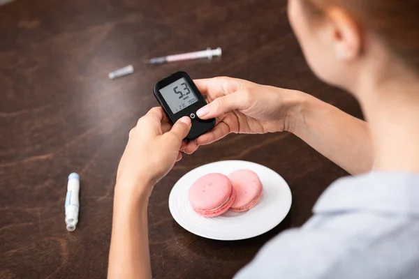 Cropped view of woman holding glucose monitor with numbers near sweet dessert — Stock Photo