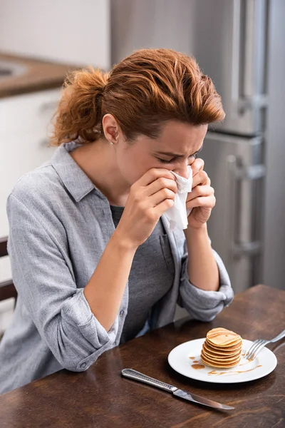 Mulher espirrando em guardanapo perto de panquecas saborosas na mesa — Fotografia de Stock