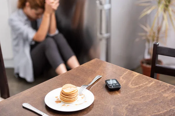 Foyer sélectif de crêpes savoureuses sur la table près du glucomètre et la femme assise sur le sol — Photo de stock