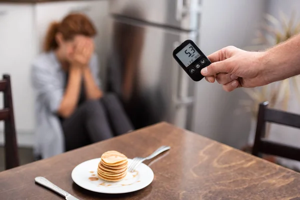 Cropped view of man holding glucose monitor with numbers near woman — Stock Photo