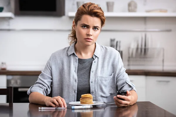 Woman with diabetes holding glucose monitor near pancakes — Stock Photo
