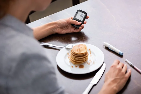 Selective focus of woman with diabetes holding glucose monitor near pancakes — Stock Photo