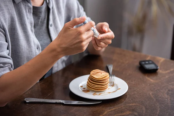 Cropped view of woman with diabetes doing blood test with blood lacet near pancakes — Stock Photo