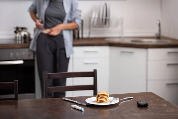 Selective focus of pancakes near medical equipment and woman in kitchen — Stock Photo