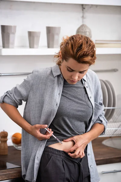 Mujer enferma parada en la cocina y haciendo la inyección con la jeringa - foto de stock