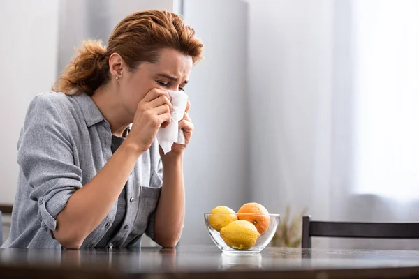 Donna con naso che cola starnutisce nel tessuto vicino all'arancia e limoni nella ciotola — Foto stock