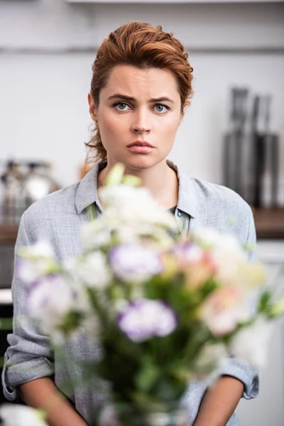 Selective focus of upset woman looking at camera near flowers — Stock Photo