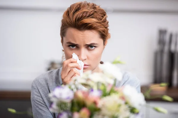 Selective focus of sick woman with pollen allergy holding tissue near flowers — Stock Photo