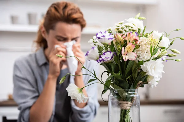 Selective focus of bouquet of flowers near woman with pollen allergy sneezing in tissue — Stock Photo