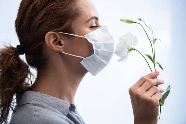 Side view of woman in medical mask smelling flowers — Stock Photo