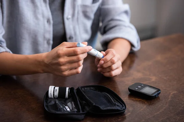 Vue recadrée d'une femme tenant une lancette de sang près d'une trousse de premiers soins — Photo de stock