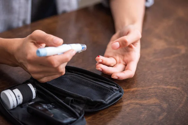 Cropped view of woman holding blood lancet near finger with blood — Stock Photo