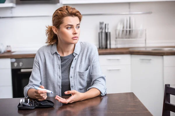 Attractive and sad woman holding blood lancet near fingers — Stock Photo