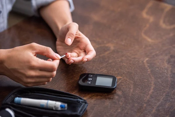 Vista ritagliata della donna che fa esami del sangue vicino al monitor glucosio — Foto stock