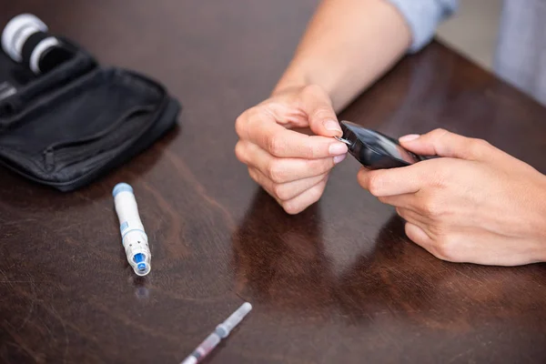 Selective focus of woman holding glucose monitor while doing blood test at home — Stock Photo