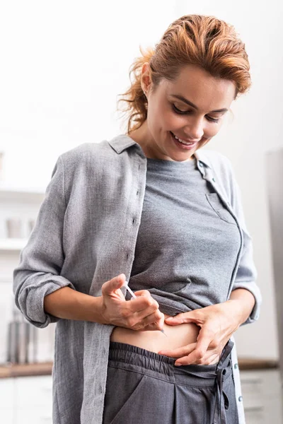 Mujer alegre de pie y haciendo la inyección con jeringa - foto de stock