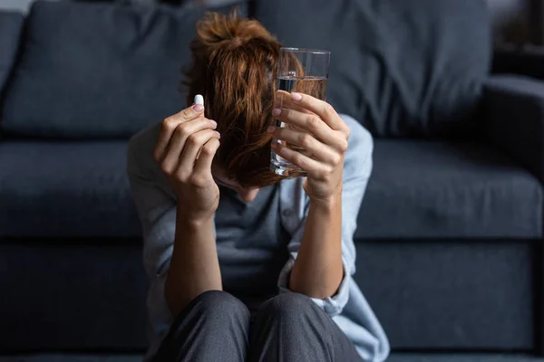Mujer enferma sosteniendo píldora y vaso de agua en casa - foto de stock