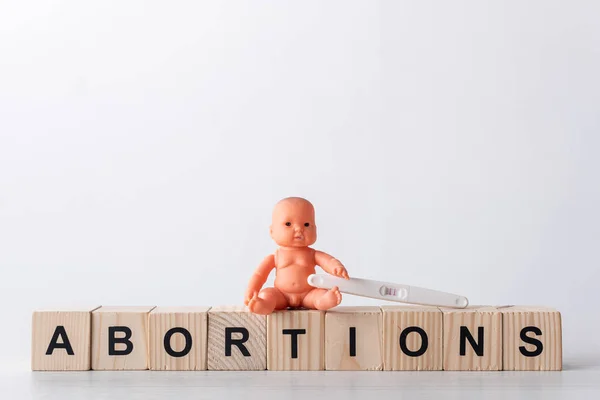 Baby doll near pregnancy test and wooden cubes with lettering on white — Stock Photo