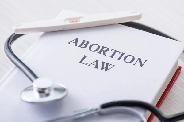 Selective focus of pregnancy test on book with abortion law lettering near stethoscope — Stock Photo