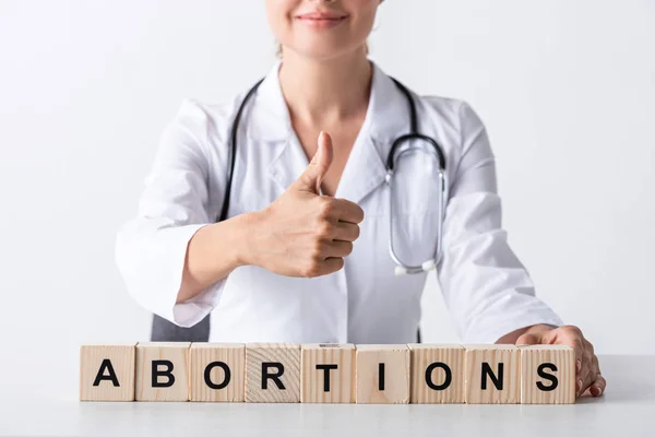 Vista recortada de médico feliz mostrando el pulgar hacia arriba cerca de cubos con cartas de aborto - foto de stock
