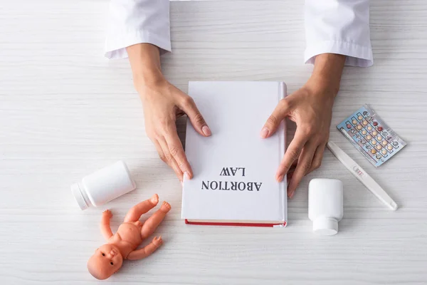 Top view of woman holding book with abortion letters near baby doll and abortion pills — Stock Photo