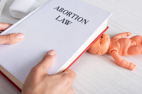 Cropped view of woman holding book with abortion lettering near baby doll — Stock Photo