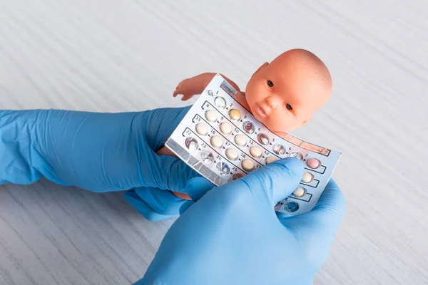 Vue recadrée du médecin dans des gants en latex tenant des pilules d'avortement et poupée dans les mains — Photo de stock