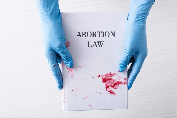 Cropped view of doctor in latex gloves holding book with abortion law letters — Stock Photo