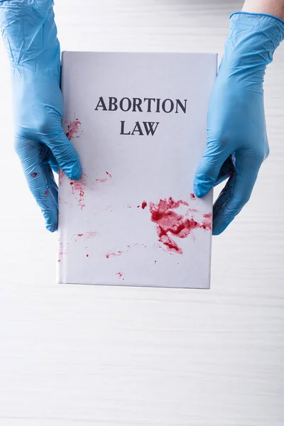 Vista dall'alto del medico in guanti di lattice in possesso di libro con lettere di legge aborto — Foto stock