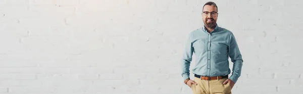 Panoramic shot of handsome and smiling businessman in shirt with hands in pockets — Stock Photo