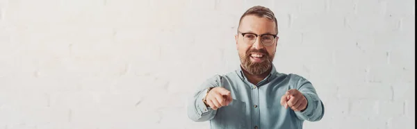 Panoramic shot of handsome and smiling businessman in shirt pointing with finger — Stock Photo