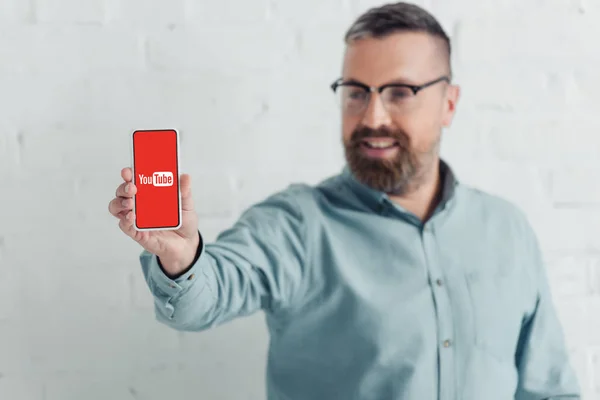 KYIV, UKRAINE - 27 de agosto de 2019: foco seletivo de belo empresário segurando smartphone com logotipo do youtube — Fotografia de Stock