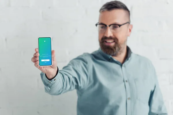 KYIV, UCRANIA - 27 de agosto de 2019: enfoque selectivo del guapo hombre de negocios que sostiene el teléfono inteligente con la aplicación de Twitter - foto de stock
