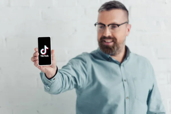 KYIV, UKRAINE - AUGUST 27, 2019: selective focus of handsome businessman holding smartphone with tik tok logo — Stock Photo