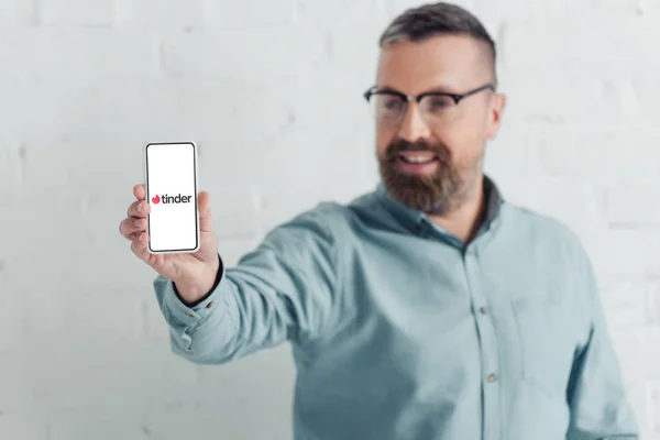KYIV, UCRAINA - 27 AGOSTO 2019: focus selettivo di un bell'uomo d'affari con smartphone con logo Tinder — Foto stock
