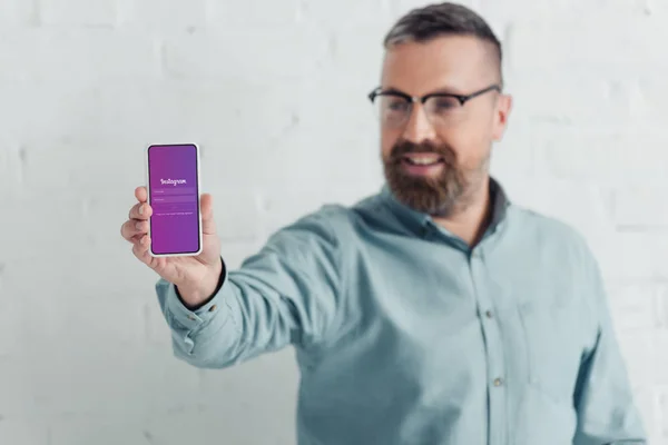 KYIV, UCRANIA - 27 de agosto de 2019: enfoque selectivo del guapo hombre de negocios que sostiene el teléfono inteligente con la aplicación instagram - foto de stock