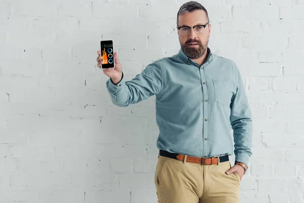 Bel homme d'affaires avec main dans la poche tenant smartphone avec graphiques et graphiques site web — Photo de stock