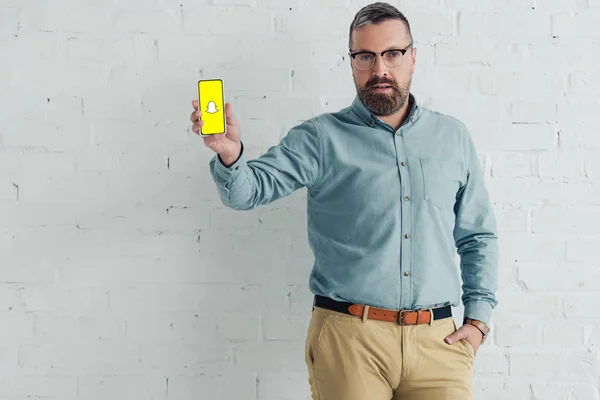 KYIV, UKRAINE - 27 AOÛT 2019 : bel homme d'affaires avec main dans la poche tenant smartphone avec logo snapchat — Photo de stock