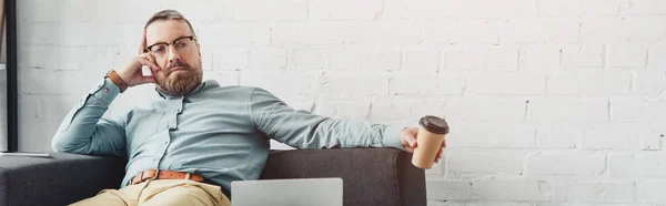 Панорамный снимок красивого бизнесмена, сидящего и держащего бумажную чашку — стоковое фото