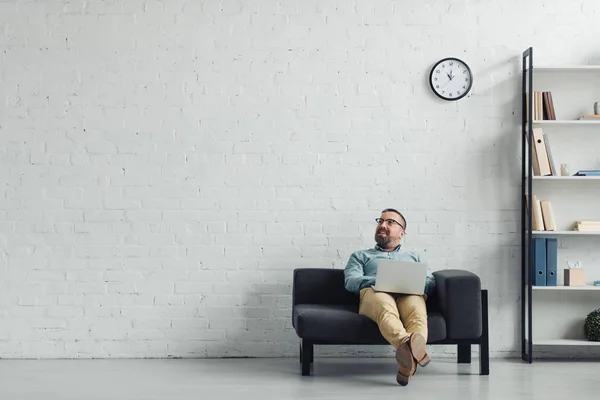 Hombre de negocios guapo en camisa que sostiene el ordenador portátil y mirando hacia otro lado - foto de stock