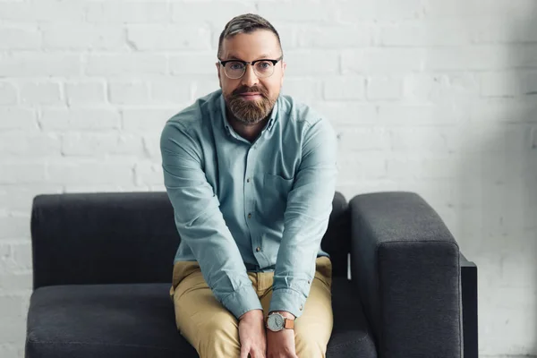 Schöner Geschäftsmann in Hemd und Brille sitzt und in die Kamera schaut — Stockfoto